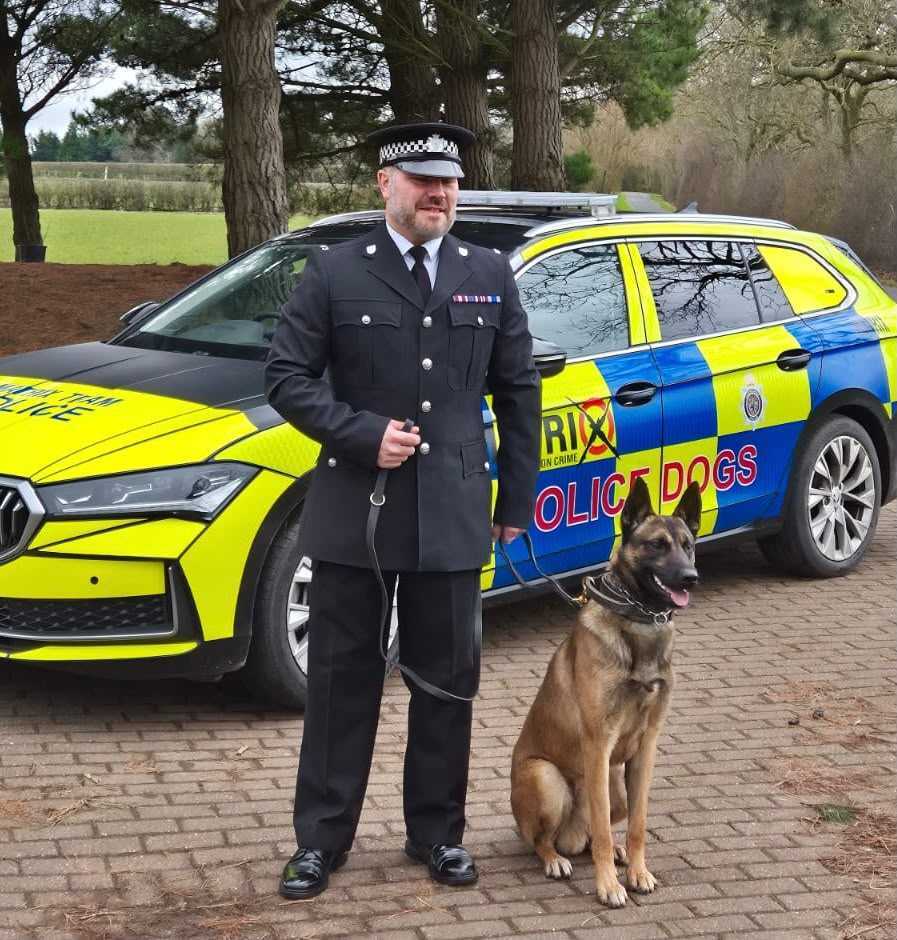 Handler in police dress uniform with a police dog beside a marked Police Dogs vehicle